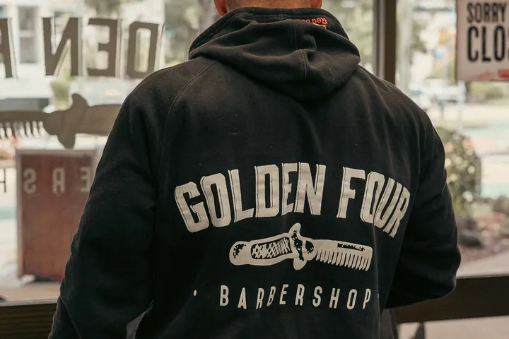 The Golden Four comb logo printed on a barber’s black hoodie